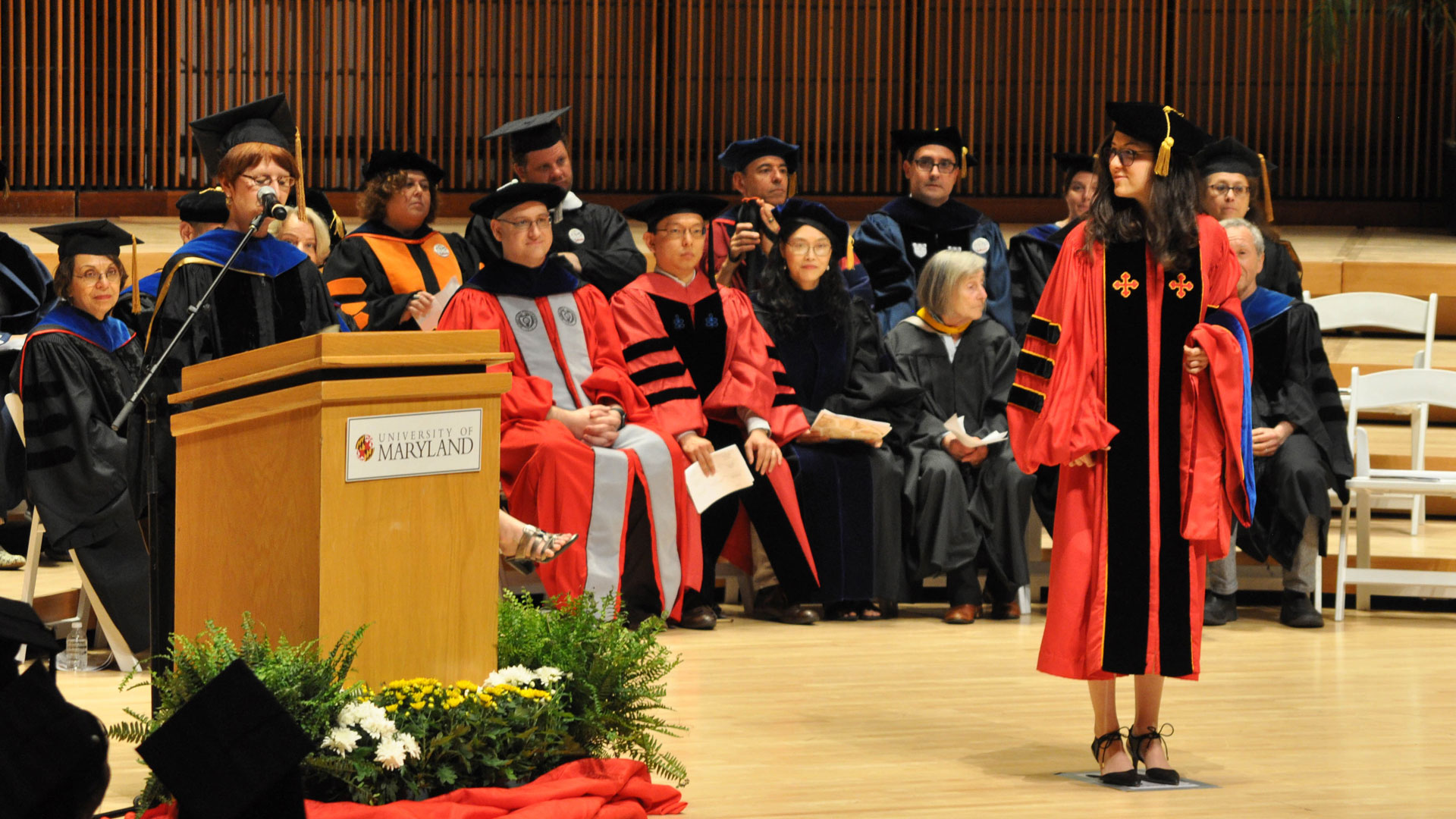 An SLLC graduate student stands on stage as they recieve their degree